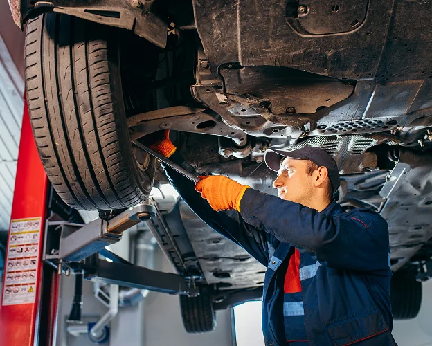 Mécanicien en gants orange réparant le dessous d'une voiture sur un élévateur Les Essarts-le-Roi dans les Yvelines 78