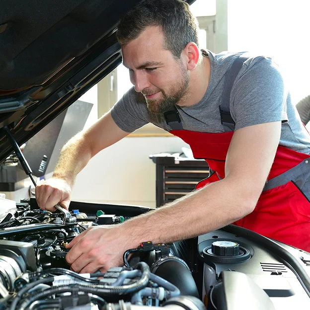 Mécanicien barbu souriant en salopette rouge, réparant le moteur d'une voiture Les Essarts-le-Roi dans les Yvelines 78