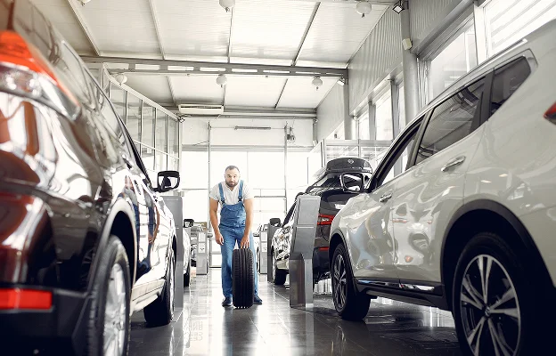 Mécanicien portant une salopette bleue transportant un pneu dans un garage de voitures Les Essarts-le-Roi dans les Yvelines 78