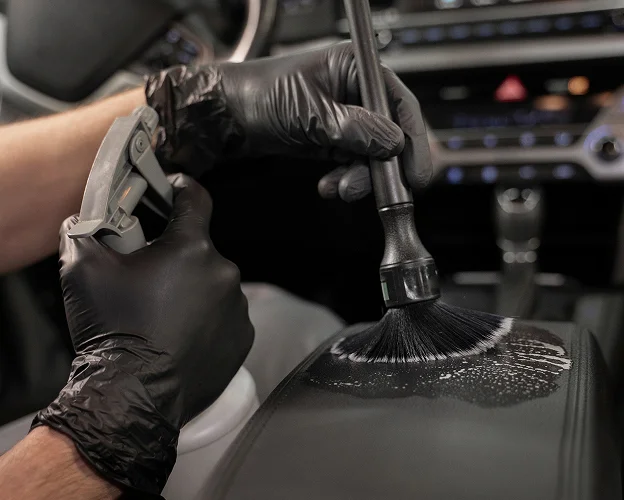 Mains gantées nettoyant l'intérieur d'une voiture avec une brosse et un spray Les Essarts-le-Roi dans les Yvelines 78