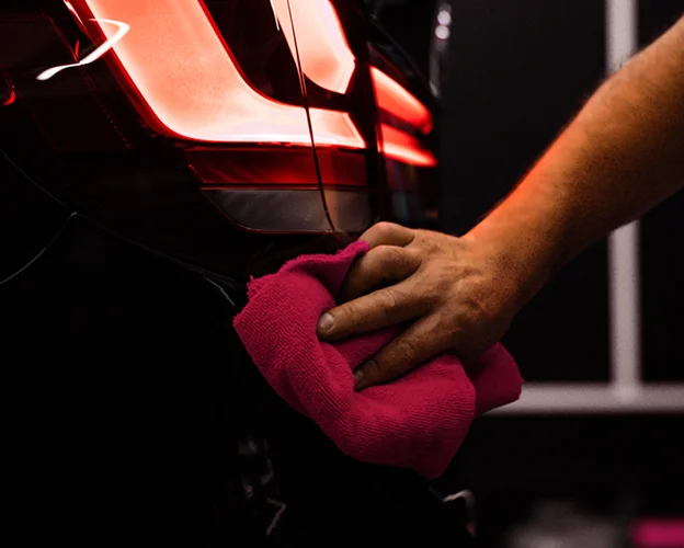 Main humaine essuyant l'arrière d'une voiture noire avec un chiffon rose Les Essarts-le-Roi dans les Yvelines 78