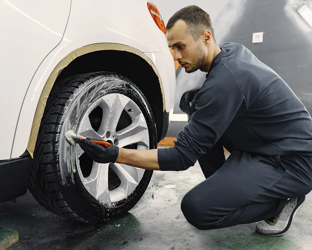 Homme nettoie une roue de voiture blanche avec une brosse et du savon Les Essarts-le-Roi dans les Yvelines 78