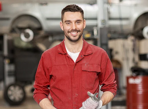 Mécanicien joyeux en combinaison rouge tenant une clé à molette dans un garage Les Essarts-le-Roi dans les Yvelines 78